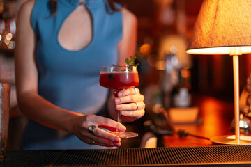 Beautiful girl bartender prepared a delicious alcoholic fresh sweet cocktail and serves it at the bar