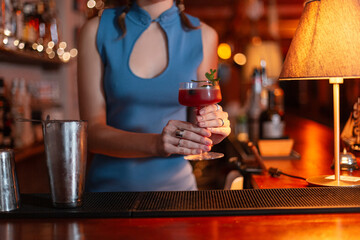 The girl bartender prepared a sweet alcoholic cocktail and serves it on the bar counter