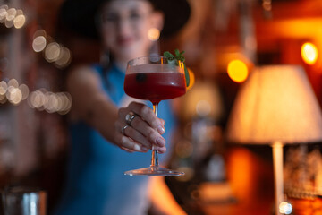 Beautiful bartender girl prepared a delicious sweet fresh alcoholic cocktail and serves it on the bar counter in the bar