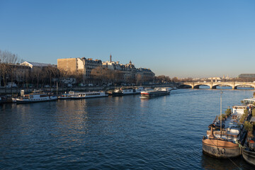Fototapeta premium Tranquil Seine river scene with boats and Parisian bridges under blue skies