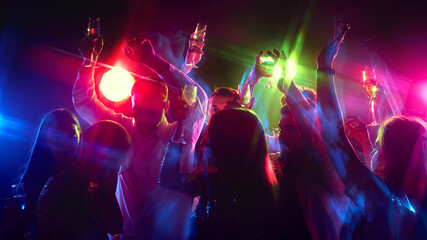 Naklejka premium Hands wave in rhythm, glasses clinking as crowd celebrates life, music, and sharing happiness under neon lights. Concept of work party, youth, carefree, celebration, winter holidays,. ad