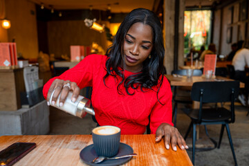 Elegant woman adding sugar to cappuccino in cafe