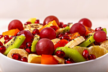 Vibrant close-up of fruit salad with kiwi, banana, grapes, persimmon, pomegranate and chia seeds in white bowl. Healthy and refreshing meal