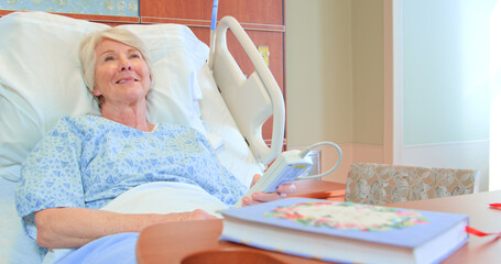 Senior Female Patient Lying In Hospital Bed Smiling As She Watches TV