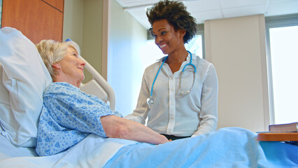 Female Doctor With Stethoscope Visiting Senior Female Patient In Hospital Bed Giving Her Good News
