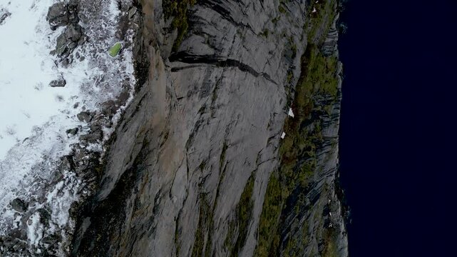 Segla prominent mountain peak on senja island, norway, showcasing steep cliffs, snow-covered slopes, and dark blue waters of the norwegian sea during winter, overhead drone and then camera titlting up