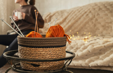 Basket full of knitting yarns and needls against sofa, woman drinking tea and relaxing at home.Empty space