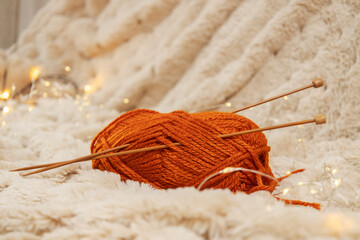 Red thread spool and wooden knitting needles on warm light brown blanket
