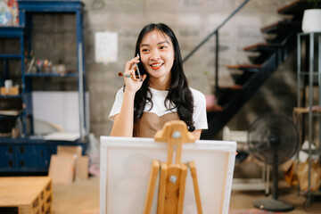 Cheerful female artist painting in a vibrant studio with brushes, a palette, and a blank canvas.