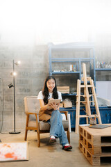 Cheerful female artist painting in a vibrant studio with brushes, a palette, and a blank canvas.