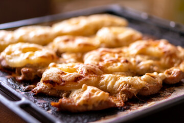 Fried chicken fillet with pineapple and cheese on a dark baking sheet