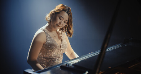 Fototapeta premium Portrait of a Talented Asian Pianist Captivating Audience with a Masterful Performance on a Grand Piano. Under Soft Stage Lights, Her Fingers Move Across the Keys, Creating Beautiful Classical Music