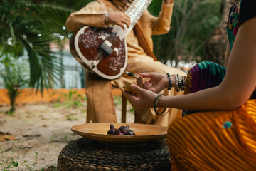 Indian musician in traditional clothes playing sitar festive season outdoor home. Woman in traditional saree hand lighting Diya lamp during Diwali festival. Happy greeting photo. Part of a series