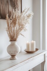 This image features a simple autumn-themed home decor arrangement. A vase with dried branches is placed on a wooden surface beside two lit candles in holders.