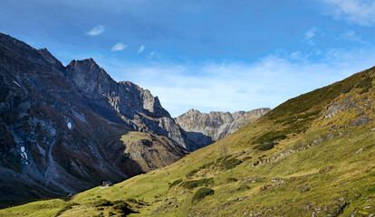 A serene mountain landscape with lush green hills and dramatic rocky peaks under a blue sky.