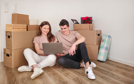 Two students sitting on the floor among moving boxes, preparing for their move to a new home.