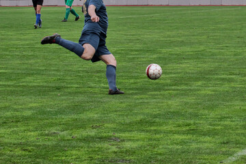 One attacking soccer player in blue uniform prepares to kick the ball, game tactics in football, footballer with the ball on the green football field close-up.