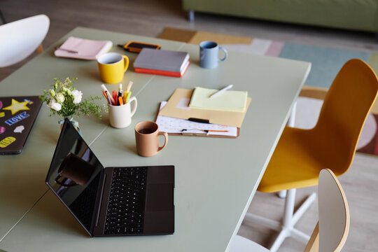 Still life shot of open laptop resting on cluttered working desk with papers and stationery in cozy office setting, copy space