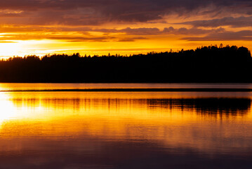 A stunning sunset over a calm lake, with dramatic clouds and warm orange and golden reflections on the water, creating a serene and scenic view.