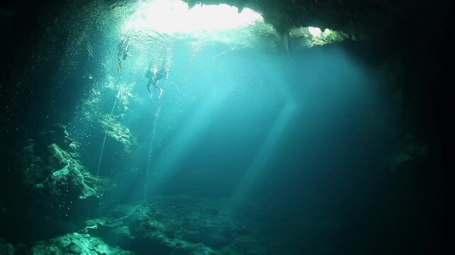 A man and a woman are swimming in a cave. The cave is dark and the water is clear