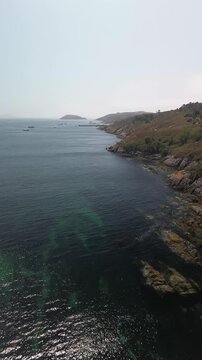 Aerial view advancing from Melide beach over the serene, crystal-clear Atlantic Ocean. Rugged, shrub-covered cliffs of Ons Island, lead to Ons harbour and Onza Island in the background. Sunny morning.