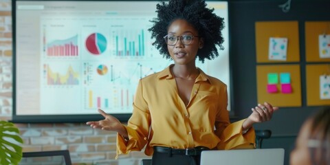 African American woman in a suit, gesturing to data visualizations on a screen.