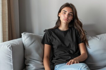 Obraz premium Young latin woman sitting on the sofa wearing a black product mock up t shirt with copy space design