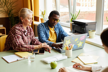 Medium shot of fashionable young Black man typing on laptop working collaboratively with