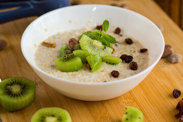 cooked oatmeal with kiwi, honey and nuts in a bowl on a wooden table