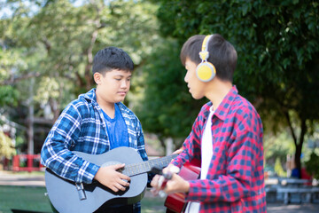 Asian boys playing and practising acoustic guitar and ukulele in school park after school together, soft and selective focus, lifestyle with musical instruments of teenagers concept.