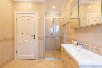 Modern Home Interior. Beige Tiled Bathroom with Bathtub and Mounted Sink Cabinet