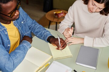 Cropped shot of African American man drawing table in notebook playing tic tac toe or noughts and crosses game with female colleague at office desk leisurely passing time, camera flash © Seventyfour