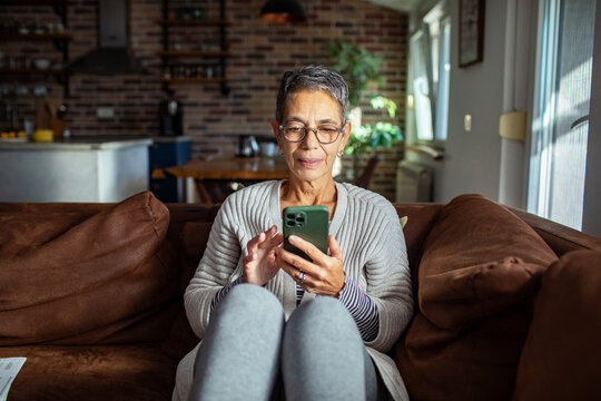 Senior woman relaxing on the couch with smartphone at home