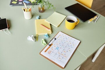 Still life shot of monthly planner with ticked off events resting on working desk cluttered with cups and office stationery at workplace