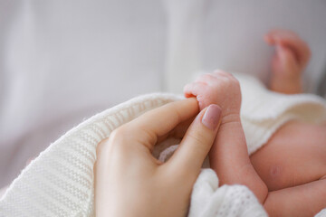 A hand holding a baby's foot. The baby is wrapped in a blanket. The baby is small and the blanket is white