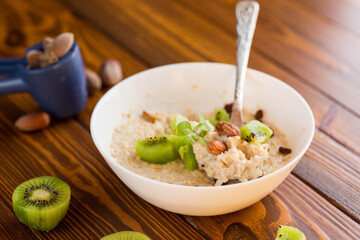 cooked oatmeal with kiwi, honey and nuts in a bowl on a wooden table