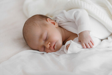 A baby is sleeping on a white blanket. The baby is wrapped in a blanket and has its head resting on its chest