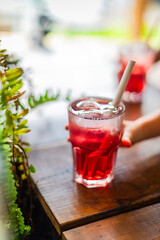 glass of refreshing red sirup cocktail with straw and hand 