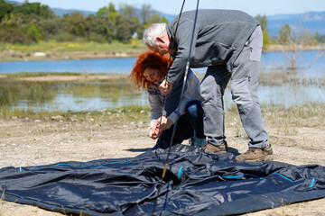 Campers setting up tent near lake on sunny day