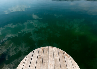Sky and Clouds reflected in the clear green water of the lake. Old wooden pier in a green lagoon.