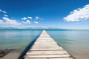 Obraz premium Wooden pier extends over calm blue waters under a bright sky in a serene coastal location