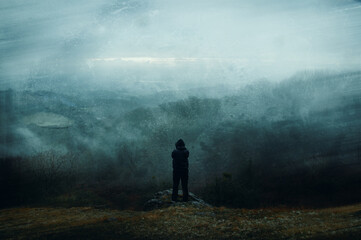 A lone hooded figure. Standing on the edge of a mountain. Onan eerie spooky winters day in the countryside. With a grunge abstract edit.