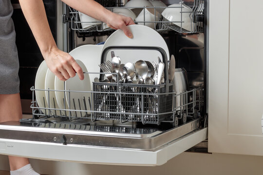 Female hand unloading dishwasher with tableware. Kitchen appliances, lifestyle view. Woman takes a plate from the dishwasher. Concept of modern technologies in the kitchen