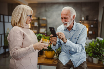 wife hold flower pot while husband photographing that with cellphone