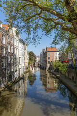 Tall Canal houses along the Oudegracht canal in Utrecht with a wharf and a bridge in the distance. A blue sky.