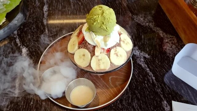 bingsu chocolate banana and red slice strawberry. matcha green tea ice cream decorative with whip cream with smoke dry ice. summer frozen cold condensed milk syrup.