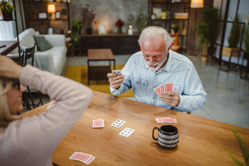 senior husband play cards with wife on wooden table at home