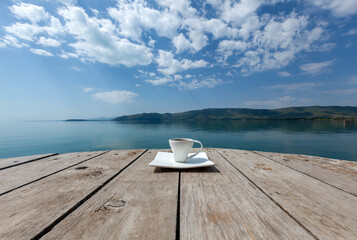 Cup of coffee on the wooden balcony and the morning lake with the blue sky