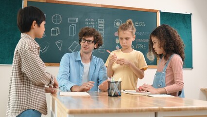 Smart teacher explain idea while diverse children drawing mind map while group of diverse student working together to do class work. Attractive instructor teaching and talking about working. Pedagogy.