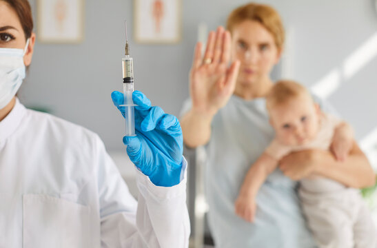 Anti-vaccine activism, mother proclaiming opposition to vaccination for newborn baby, stop immunization shot on childhood vaccine schedule in clinic by pediatrician doctor to protect small child 